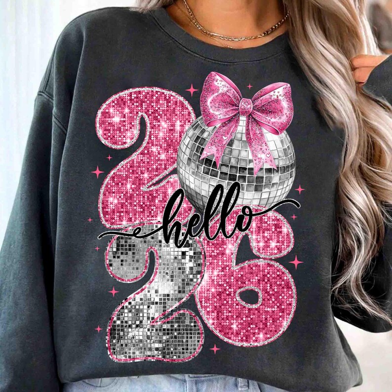 May include: Dark gray sweatshirt featuring a sparkly pink "26" design with a disco ball and pink bow. The word "hello" is written in cursive. Pink star accents complete the design.