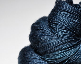 May include: A close-up of a skein of dark blue yarn. The yarn is tightly wound, with visible strands and a slight sheen. The yarn is a deep, rich shade of blue, with subtle variations in tone.