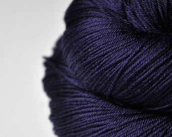 May include: Close-up of a skein of dark purple yarn. The yarn is tightly wound, with visible individual strands and a subtle sheen. The background is plain white, accentuating the yarn's texture and colour.