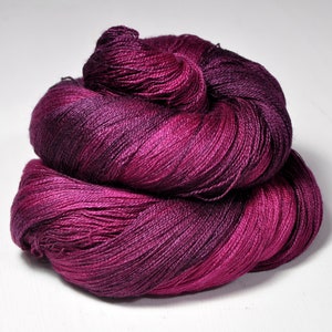 Op de afbeelding: Een streng handgeverfd garen in tinten diep paars en magenta. Het garen is strak opgewonden en onthult een kleurovergang van donker naar licht. Ideaal voor breien, haken of andere textielkunstprojecten.