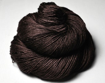 May include: A single, tightly wound skein of dark brown yarn. The fiber has a subtle, smooth sheen and a consistent, fine-plied texture throughout the entire bundle, which is coiled into a rounded, voluminous shape with visible individual strands.