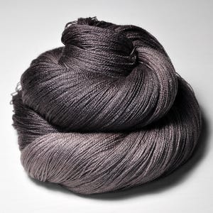 Peut inclure: Pelote de fil gris foncé, avec un dégradé subtil vers un gris argenté plus clair. Le fil est finement filé, avec une texture lisse et légèrement brillante. Idéal pour les projets de tricot ou de crochet.