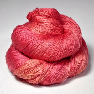 May include: A skein of vibrant, hand-dyed yarn in shades of red and coral. The yarn is tightly wound, showcasing a smooth texture and subtle color variations. Ideal for knitting or crochet projects, this yarn adds a pop of color to any craft.