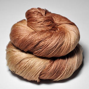 Peut inclure: Gros plan sur deux écheveaux de fil de couleur marron et beige. Le fil est étroitement enroulé, avec des brins visibles créant un aspect texturé. Les couleurs se fondent en douceur, créant un effet de dégradé. Idéal pour les projets de tricot ou de crochet.