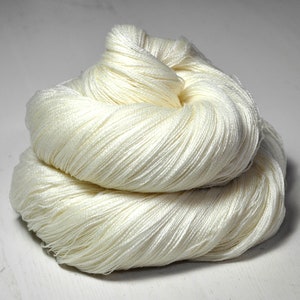 May include: A skein of white yarn, made of natural fibers, is shown in a close-up view. The yarn is soft and fluffy, and it is perfect for knitting or crocheting.