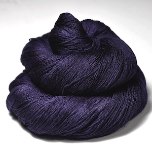 Peut inclure: Une grosse pelote de fil violet foncé, étroitement enroulée et texturée. Le fil semble doux et luxueux, avec un léger éclat. La couleur est une nuance de violet profond et riche, adaptée aux projets de tricot ou de crochet.