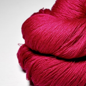 Op de afbeelding: Close-up van twee strengen levendig fuchsia garen. Het garen is strak opgerold en toont afzonderlijke strengen. De textuur lijkt zacht en glad, ideaal voor brei- of haakprojecten. De achtergrond is effen wit.