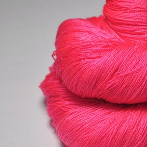 May include: A close-up of a bright pink skein of yarn. The yarn is soft and fluffy, and it is perfect for knitting or crocheting.