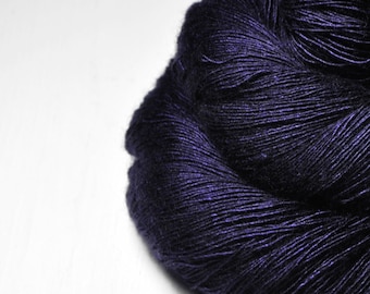 May include: A close-up of a skein of dark purple yarn. The yarn is tightly wound and has a slightly shiny texture. The background is plain white.
