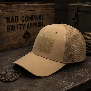 May include: A tan baseball cap featuring a solid front panel with a rectangular hook-and-loop patch area for attachments, a curved brim, and a breathable mesh back panel. The cap is constructed with a durable ripstop fabric on the front and crown.