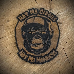 May include: A brown and black patch featuring a gorilla wearing a cap and sunglasses. The text "NOT MY CIRCUS" arches above the gorilla, and "NOT MY MONKEYS" arches below.