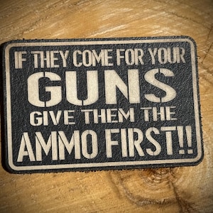 May include: A rectangular black and tan patch with the text "IF THEY COME FOR YOUR GUNS GIVE THEM THE AMMO FIRST!!" in bold white letters. The patch has a textured appearance and a dark border.