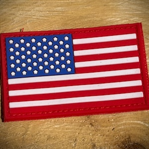 May include: A rectangular patch depicting the American flag. It has a red border, a blue canton with white stars, and red and white stripes. The patch is a patriotic emblem.