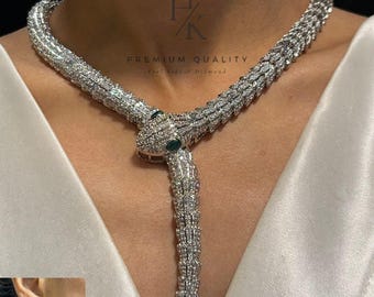 May include: A diamond-encrusted snake necklace with matching earrings. The necklace wraps around the neck and features a snake head with green gemstone eyes. The earrings mirror the necklace design. The jewelry is set against a white background.