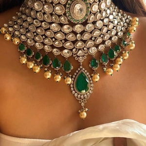 Puede incluir: Un collar llamativo y lujoso con un diseño en capas con piedras preciosas claras y verde esmeralda. El collar tiene un colgante central en forma de lágrima verde esmeralda y está adornado con cuentas doradas. Una joya impresionante.