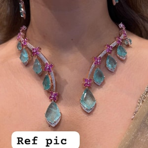 Könnte beinhalten: Ein Halsketten- und Ohrringset aus roségoldfarbenem Metall mit hellblauen tropfenförmigen Steinen und kleinen rosa Blumenakzenten. Die Halskette hat ein geschwungenes Design mit abwechselnden blauen Steinen und rosa Blüten, besetzt mit winzigen weißen Steinen.