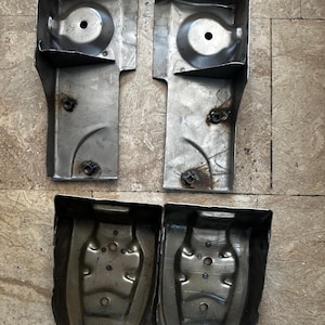 May include: Four metal automotive parts. Two are rectangular with a curved top and a circular indentation. The other two are curved, with multiple holes and a rounded shape. All parts are silver and appear used.