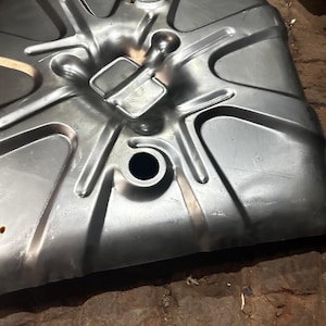 May include: A silver-colored, stamped metal component with multiple circular and rectangular openings. The piece has a series of raised ridges and a curved shape. The item appears to be a part of a larger mechanical assembly.