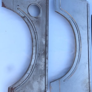 May include: Two vintage, unpainted metal car body panels. The panels are curved with a circular hole and various stamped details. The metal has a weathered appearance with some rust, suggesting age and use. The panels are likely for restoration projects.