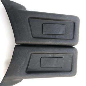 Puede incluir: Dos molduras de plástico negro para automóviles. Cada pieza tiene un área rectangular empotrada y un diseño curvo y en ángulo. Es probable que las piezas sean para el interior o el exterior de un vehículo.