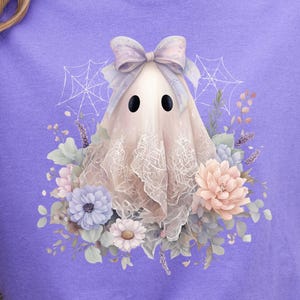 May include: Violet-colored t-shirt featuring a ghost graphic. The ghost is adorned with a bow and lace, surrounded by flowers and spiderwebs. The word "VIOLET" is printed at the top. A comfortable, casual tee for Halloween.