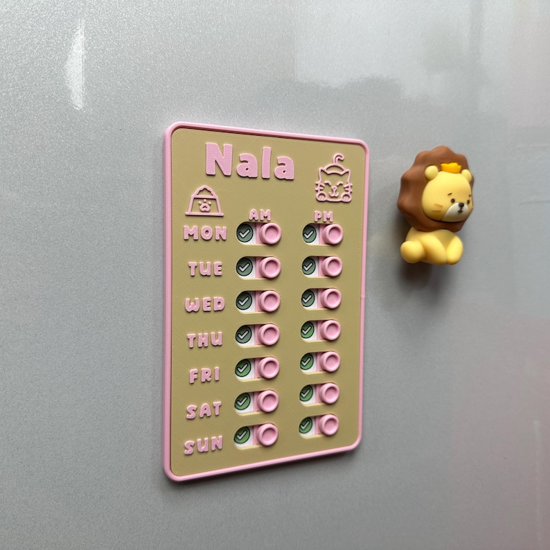 May include: A magnetic weekly planner with the name "Nala" in pink lettering. The planner has a light brown background with pink borders and features a lion-shaped magnet. The planner includes AM and PM check boxes.