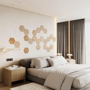 Op de afbeelding: Een moderne slaapkamer met een neutraal kleurenpalet. Het bed heeft wit beddengoed en een grijs hoofdbord. Houten zeshoekige wanddecoratie en een stijlvolle lamp. Een nachtkastje met een lamp en een boek staat naast het bed.
