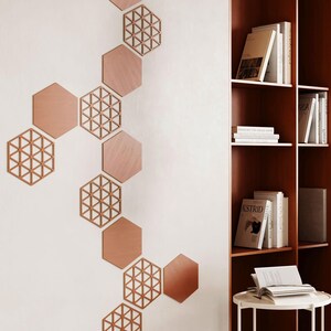 May include: A collection of wooden hexagon wall decor in varying designs and shades of brown. Some hexagons are solid, while others feature an open, geometric pattern. The decor is arranged on a white wall, creating a modern, artistic display.