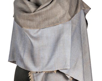 May include: A two-tone shawl draped over a mannequin. The top layer is a muted brown, while the lower section is a light blue-gray. The shawl has a fringed edge and is made of a soft, flowing fabric.
