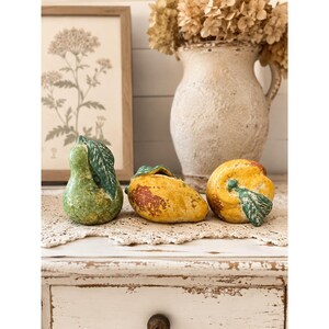 Può includere: Tre statuette decorative di frutta in ceramica che includono una pera verde testurizzata con una foglia, un mango giallo con una foglia verde e una pesca gialla rotonda con una foglia verde. Ogni pezzo ha una finitura invecchiata e usurata.