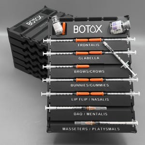 May include: Black plastic organiser with the word "BOTOX" in white. The organiser holds syringes and vials, labelled for facial areas such as Frontalis, Glabella, and Brows/Crows. The syringes have orange plungers.