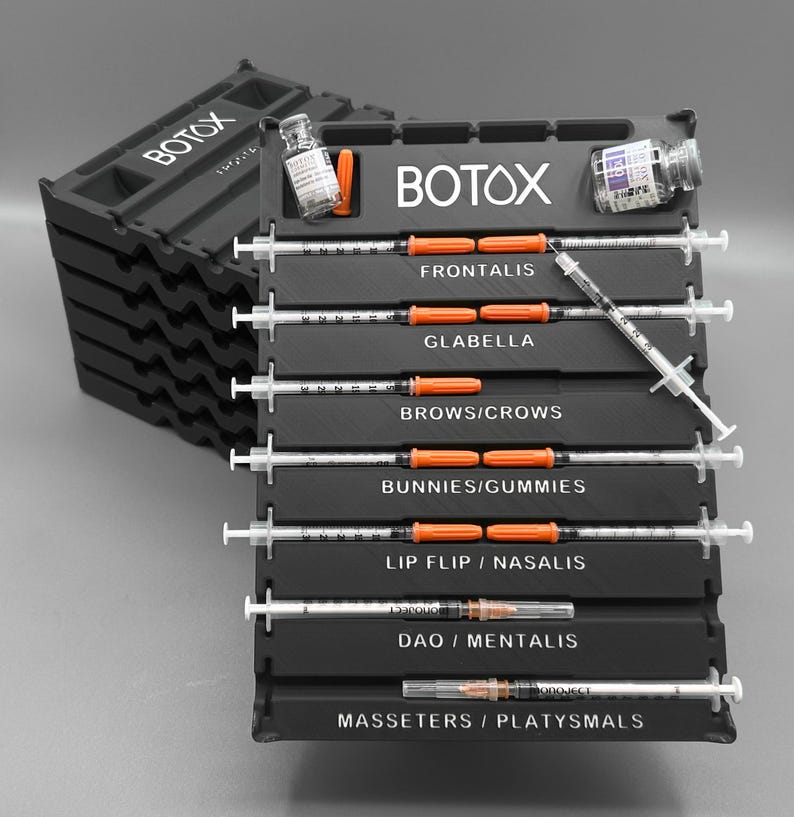 May include: Black plastic organizer with the word "BOTOX" in white. The organizer holds syringes and vials, labeled for various facial areas like Frontalis, Glabella, and Brows/Crows. The syringes have orange plungers.