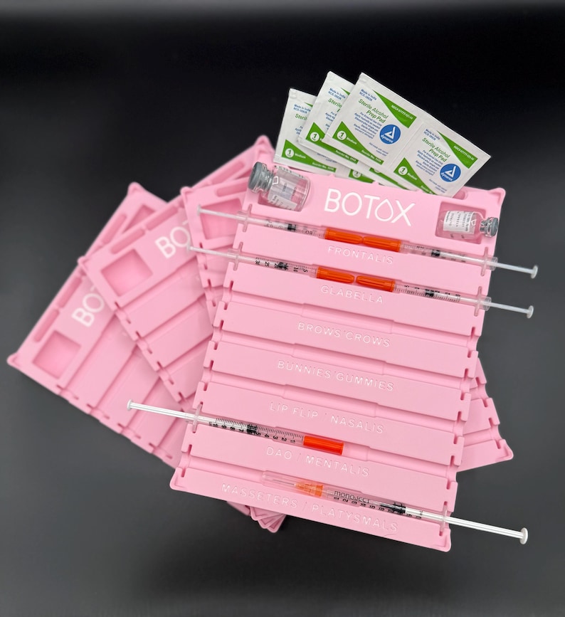 May include: Pink plastic trays with the word "BOTOX" printed on them. Each tray has slots for syringes and vials. Syringes are filled with an orange liquid. Alcohol prep pads and vials are also visible.