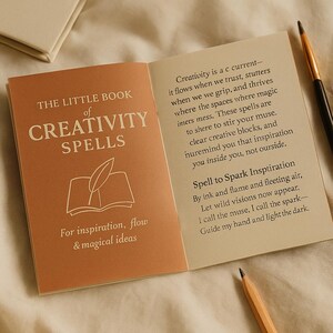 May include: An open book titled "THE LITTLE BOOK of CREATIVITY SPELLS" with text and illustrations. The cover is a muted orange color. A paintbrush and pencil are visible.