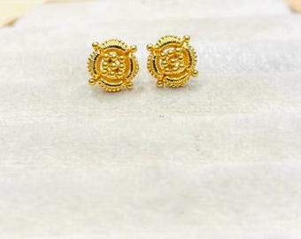 May include: A pair of gold-colored stud earrings. Each earring features a circular design with intricate detailing, including a central cluster of small beads and a decorative outer ring. The earrings have a polished finish.
