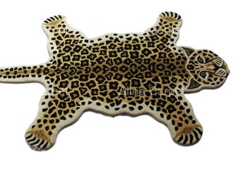 May include: A beige and brown leopard print rug shaped like a leopard skin. The rug has a cream-colored background with brown spots and a detailed head and paws. The rug is designed to resemble a leopard skin.
