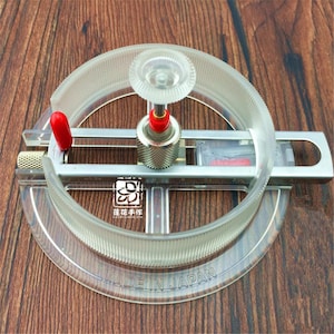 May include: A clear, circular circle cutter with a red handle and a silver metal base. The cutter has a clear plastic ring with measurement markings and the text "MADE IN JAPAN". The tool is designed for precision cutting.