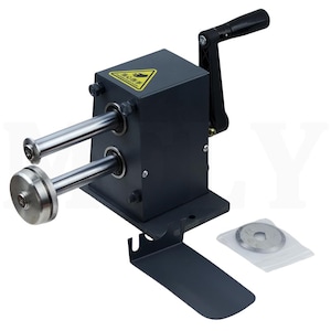May include: A black metal manual paper cutter with a hand crank and two silver rollers. A yellow warning sign is on the top. A small plastic bag with a circular blade is next to the cutter.