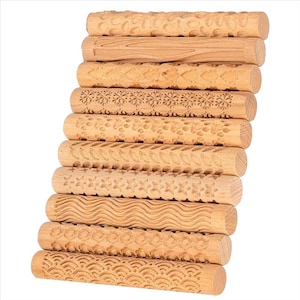 May include: A stack of ten wooden rolling pins with various carved patterns. Designs include floral, snowflake, and geometric shapes. The rolling pins are made of light-colored wood and are arranged vertically against a white background.