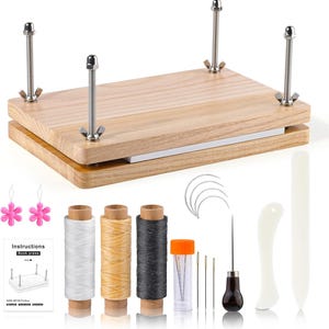 May include: A wooden book press with four metal bolts and wingnuts, accompanied by spools of thread, needles, and other bookbinding tools. The kit includes a small instruction booklet and pink flower-shaped charms.