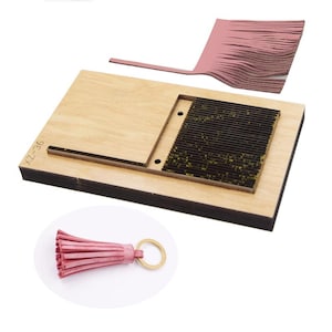 May include: A wooden die-cut machine with a rectangular base and a section for cutting. A pink leather tassel keychain is in the foreground. The die-cut machine has the text "XZ-36" on the side. A pink leather piece is also included.