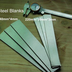 May include: A collection of DC53 steel blanks, with dimensions of 250mm x 40mm x 4mm and 220mm x 30mm x 3mm, are displayed on a wooden surface. A dial caliper rests on top. The text "DC53 Steel Blanks" is visible.