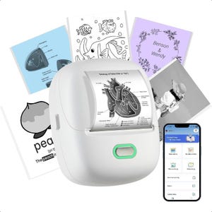 May include: A white pocket printer with a green button, printing a diagram of a heart. Several printed cards surround the printer, including a peach illustration, a fish drawing, and a photo. A smartphone displays the printer's app.