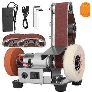 Puede incluir: Una lijadora de banda de sobremesa plateada y negra con una banda de lijado marrón, una rueda de pulido y una muela abrasiva. Incluye una fuente de alimentación, bandas de lijado adicionales y llaves Allen. La lijadora tiene un interruptor.
