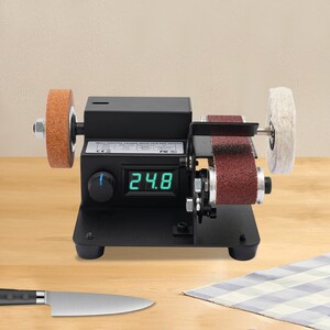 A digital rotary tool with a spinning wheel and a display showing the time, placed on a wooden surface next to a knife.
