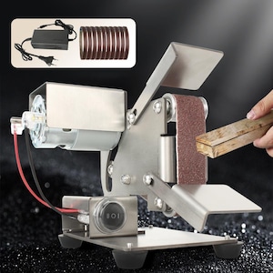 May include: A silver-colored belt sander with a brown sanding belt. The sander has a motor, power switch, and is shown with a wooden block being sanded. A power adapter and extra sanding belts are also included.