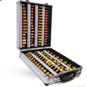 May include: An open, silver metal toolbox filled with various yellow and red router bits. The bits are organized in rows and columns, with a black handle and latches. The toolbox is on a white background.