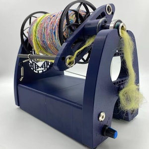 May include: A navy blue spinning wheel with a colorful yarn skein. The wheel has a black flywheel and a control knob with numbers. Yellow fiber is being spun from the yarn. The wheel is designed for fiber art and yarn crafts.