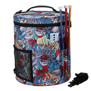 May include: A round knitting bag with a black handle and a colorful floral pattern in shades of blue, red, and yellow. The bag has multiple pockets, including a mesh side pocket and a pocket for knitting needles. Knitting needles are visible in the side pocket.