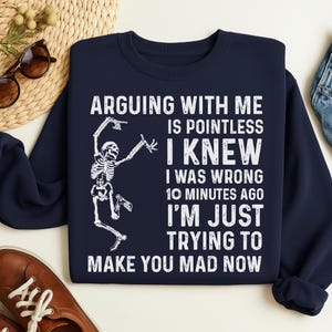 May include: Navy blue sweatshirt with white text and a skeleton graphic. The text reads: "ARGUING WITH ME IS POINTLESS I KNEW I WAS WRONG 10 MINUTES AGO I'M JUST TRYING TO MAKE YOU MAD NOW."